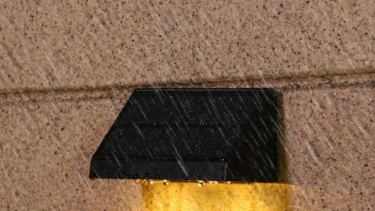 Solar wall light mounted outdoors with rain running over its sealed waterproof housing